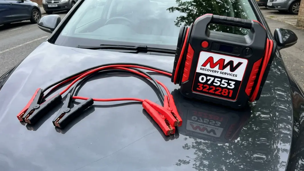 Jump leads and portable jump starter pack laid out ready to use on a car bonnet in Manchester