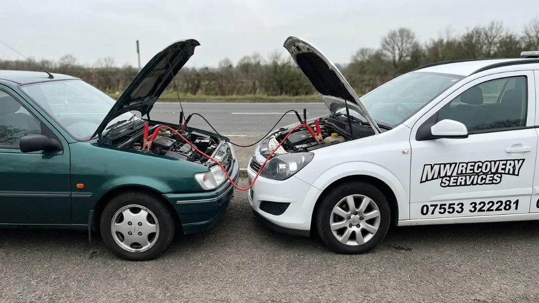 Two cars with jump leads connected showing red and black cables routed between batteries